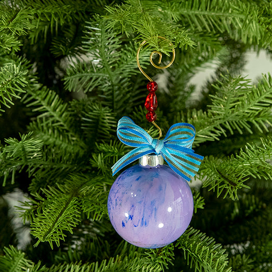 The Shelby Hand Painted Glass Ball Ornament is lavender and blue with a hint of gold metallic, silver shimmer and a blue striped shimmer ribbon. Painted using fluid acrylic and acrylic paints. Displayed on a Christmas tree.