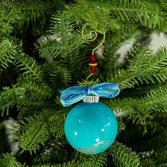 The Courtney Hand Painted Glass Ball Ornament is turquoise blue with metallic silver, white, silver shimmer and a blue striped shimmer ribbon. Painted using fluid acrylic and acrylic paints. Displayed on a Christmas tree.